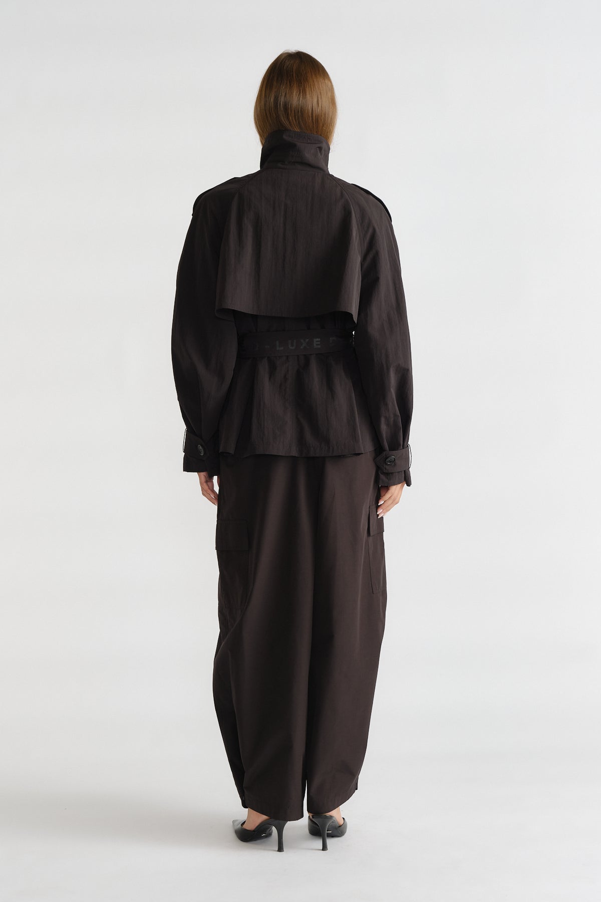 Back view of woman wearing a cropped black nylon trench jacket with a belted waist and wide-legged pants