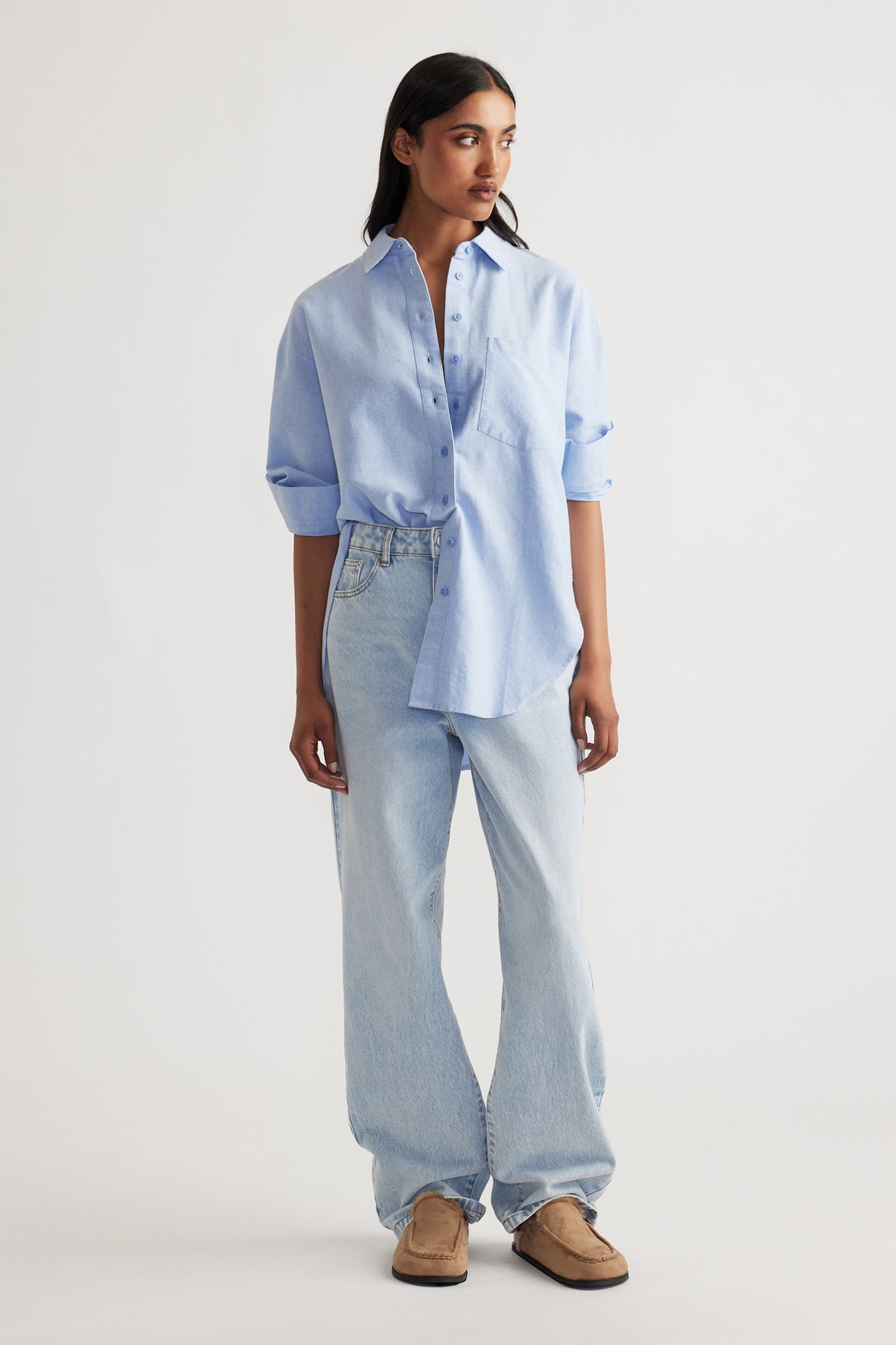 Woman wearing a relaxed light blue oversized shirt paired with loose light wash denim jeans and tan slip-on shoes