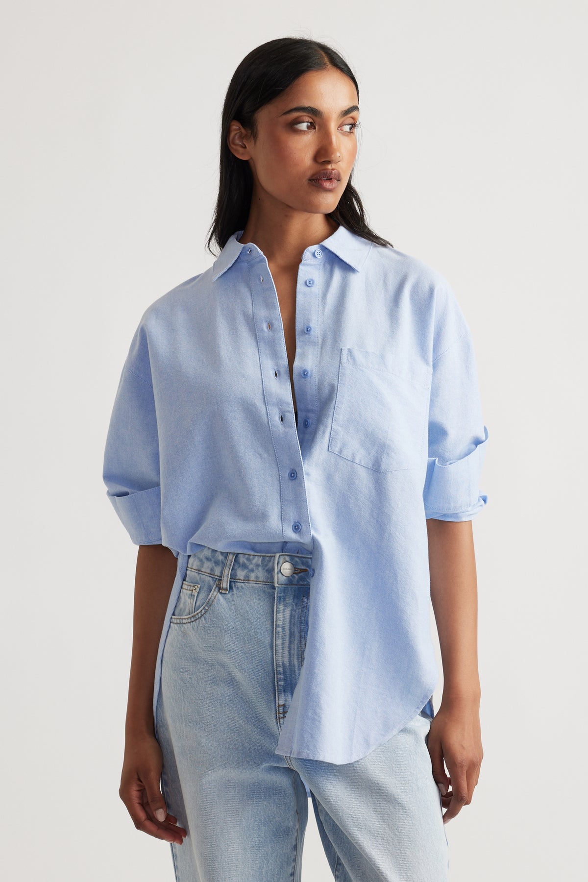 Woman wearing a light blue oversized shirt with rolled sleeves and a front chest pocket paired with light wash jeans