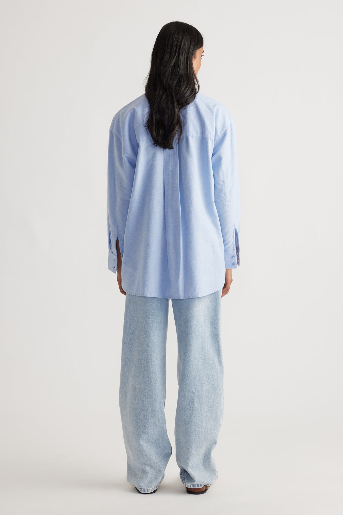 Back view of a light blue oversized shirt paired with relaxed wide-leg light-wash denim jeans for a casual look