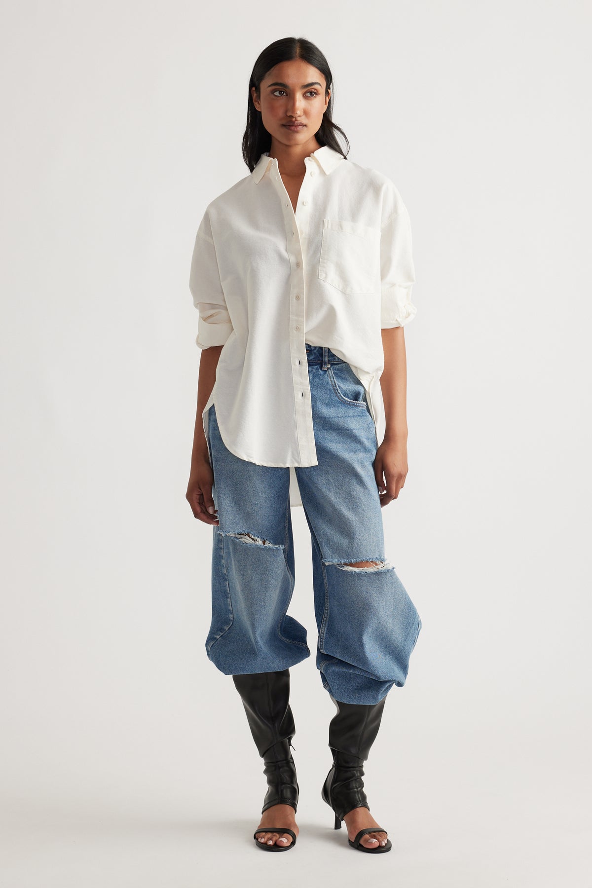 Woman wearing an oversized light oxford shirt with relaxed fit ripped wide-leg denim jeans and black heeled boots