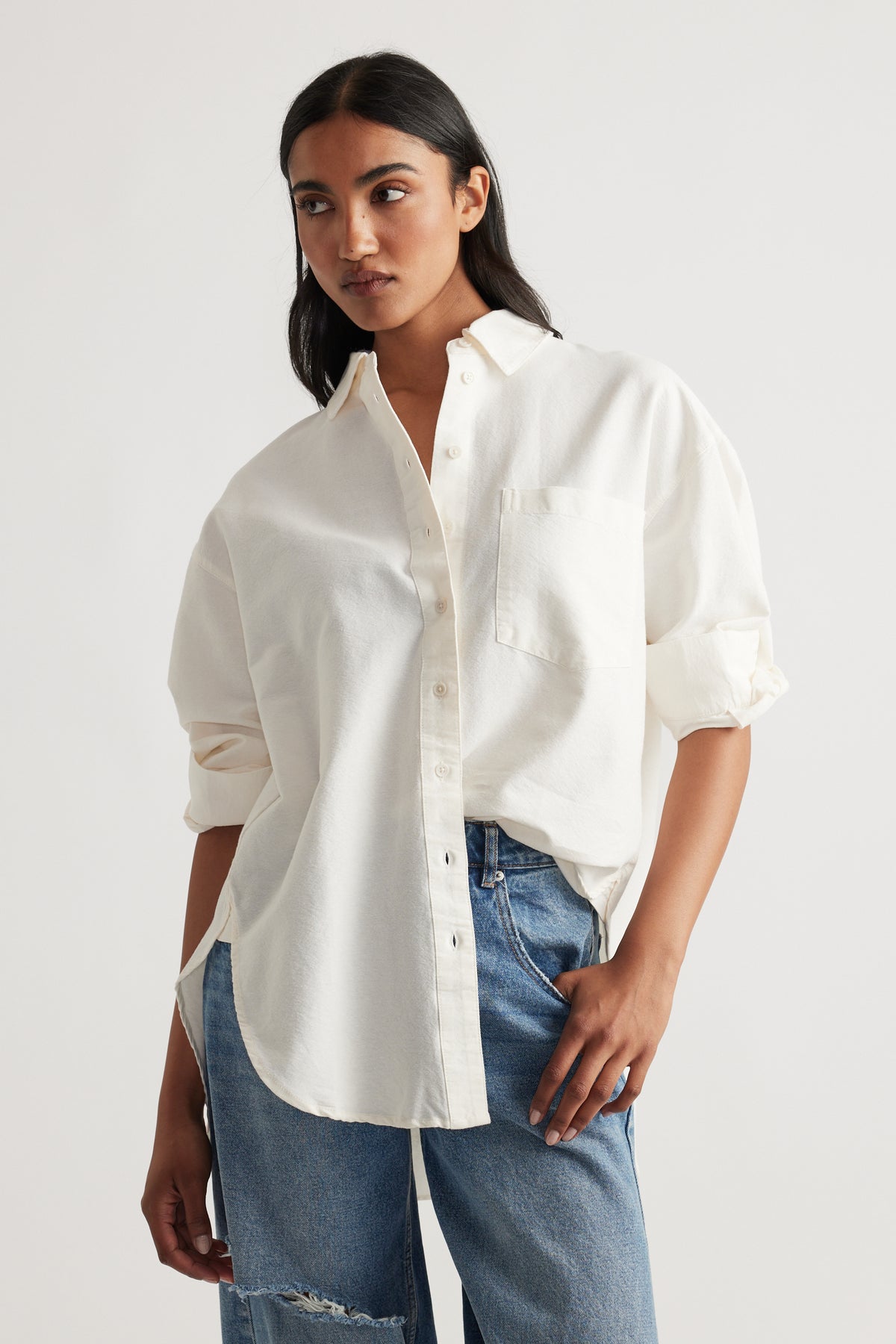Relaxed fit warm white oversized shirt with rolled sleeves, styled with distressed blue denim jeans for a laid-back look