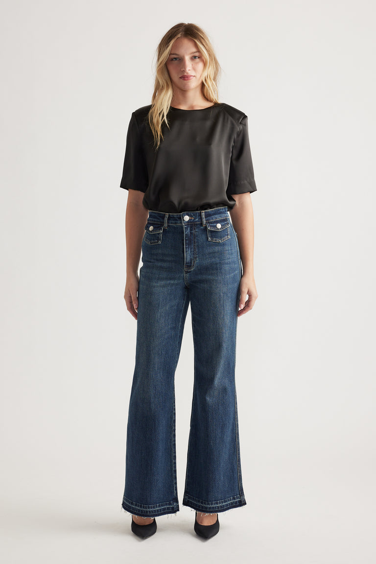 Woman wearing dark wash flare jeans paired with a black short-sleeve satin top and black pointed heels