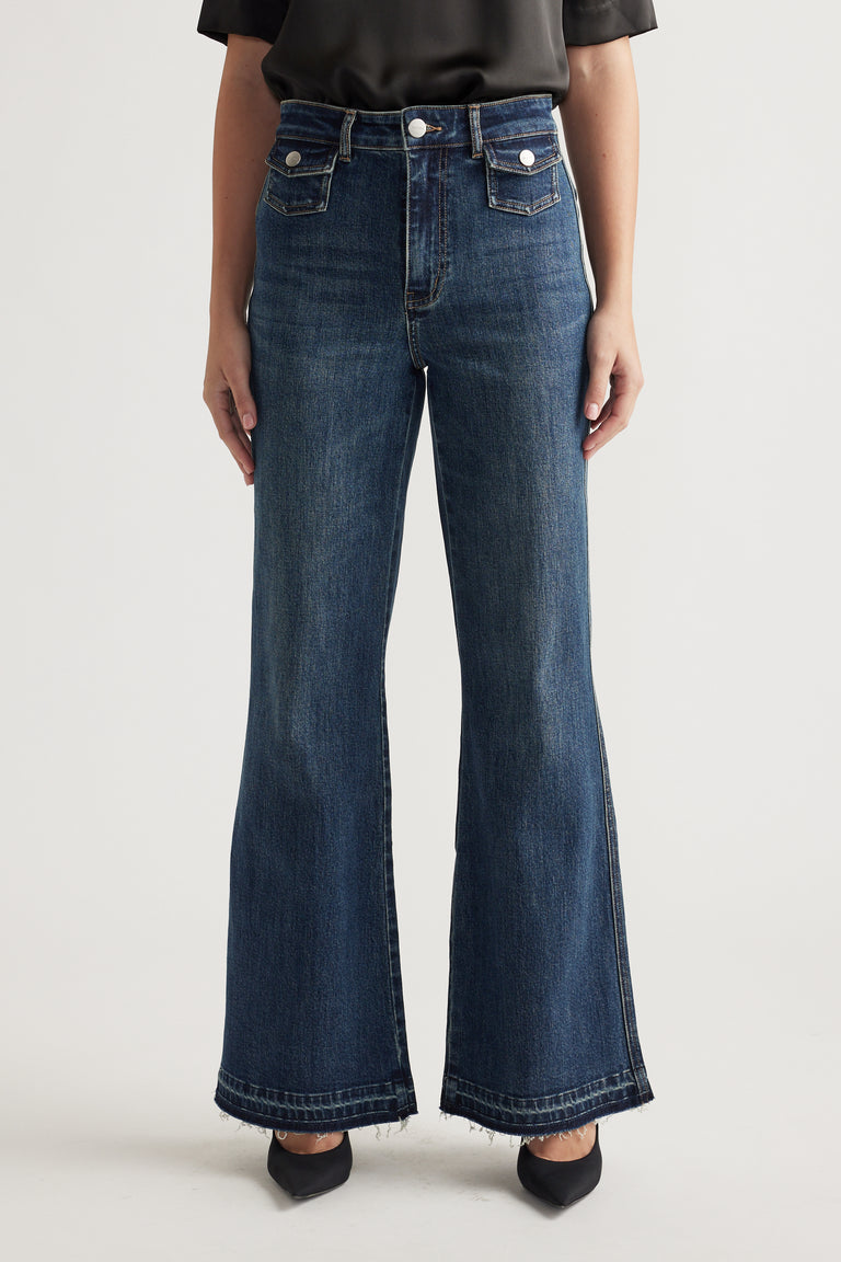 Woman wearing dark blue high-waisted flare jeans with front flap pockets and a black top paired with black pointed flats.