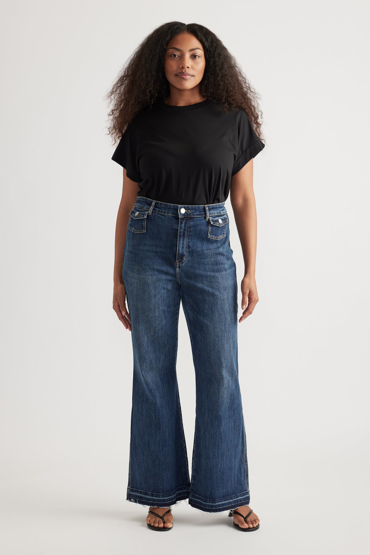 Woman wearing high rise blue flare jeans with a black tee and sandals