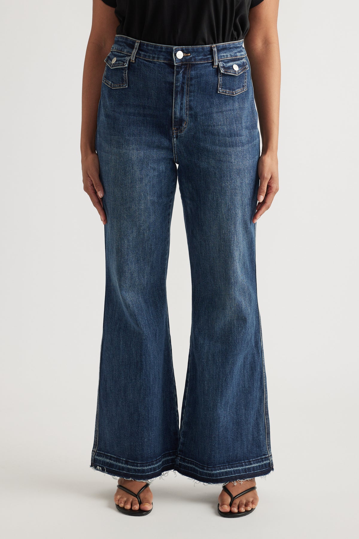 Woman wearing high rise dark blue flared jeans with frayed hems and sandals