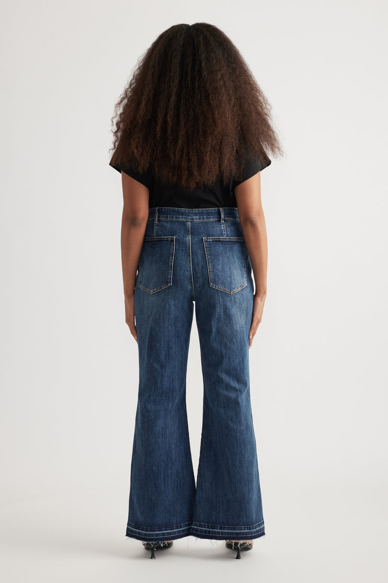 Back view of woman in a black top and high rise full length dark blue flared jeans with back pockets