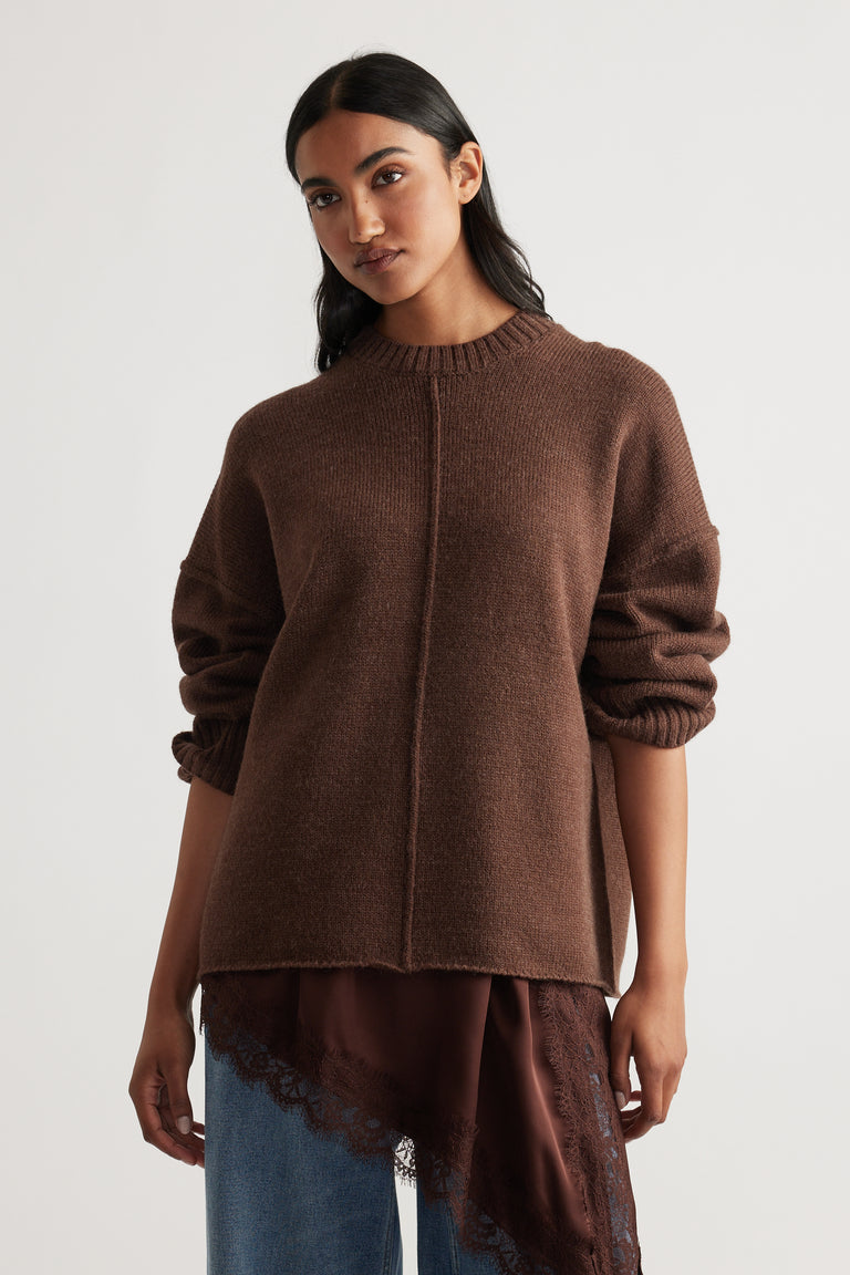 Cozy brown knit jumper with central seam, relaxed fit, and paired with layered lace-trimmed satin top and blue jeans