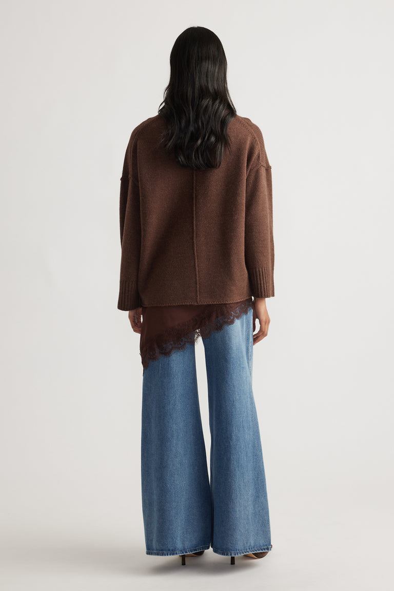 Back view of a relaxed brown knit jumper with seam detail layered over a lace-trimmed top and wide-leg blue denim jeans