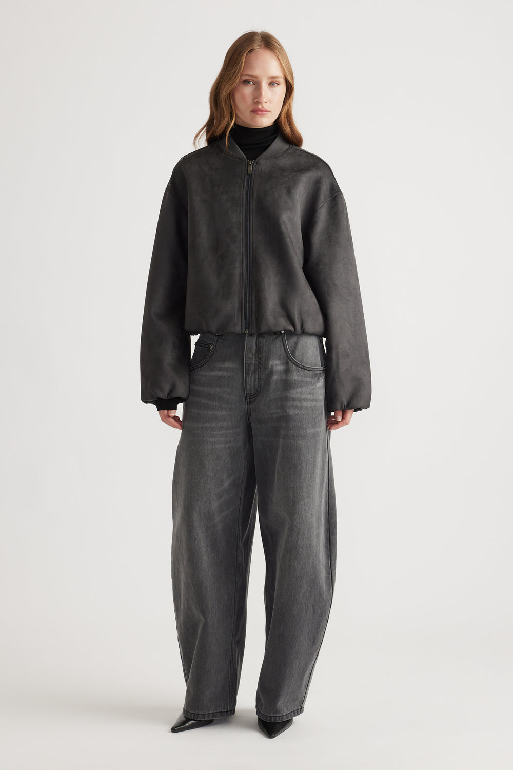 Woman wearing Eden Faux Suede Bomber Jacket in charcoal paired with wide-leg dark denim jeans and black turtleneck.