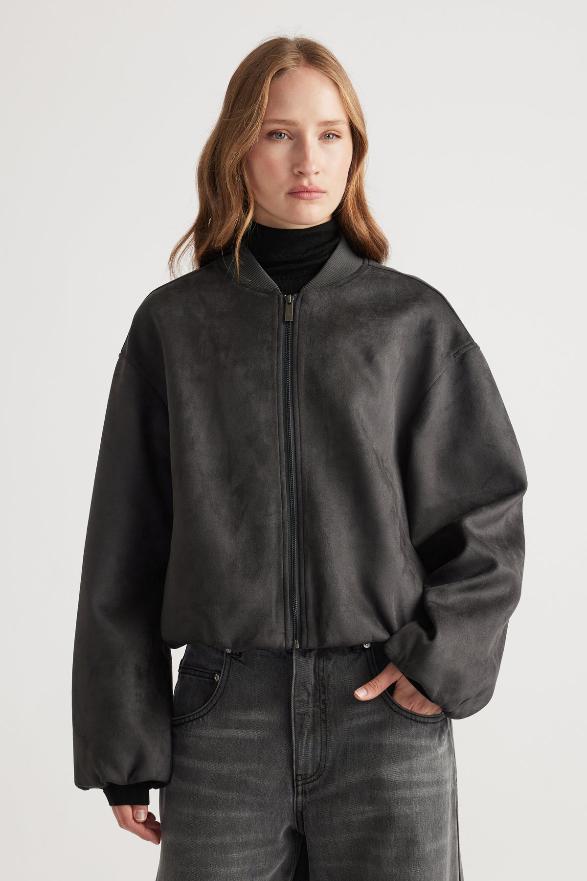Woman wearing a charcoal Eden Faux Suede Bomber Jacket styled with black turtleneck and washed black jeans for a modern look