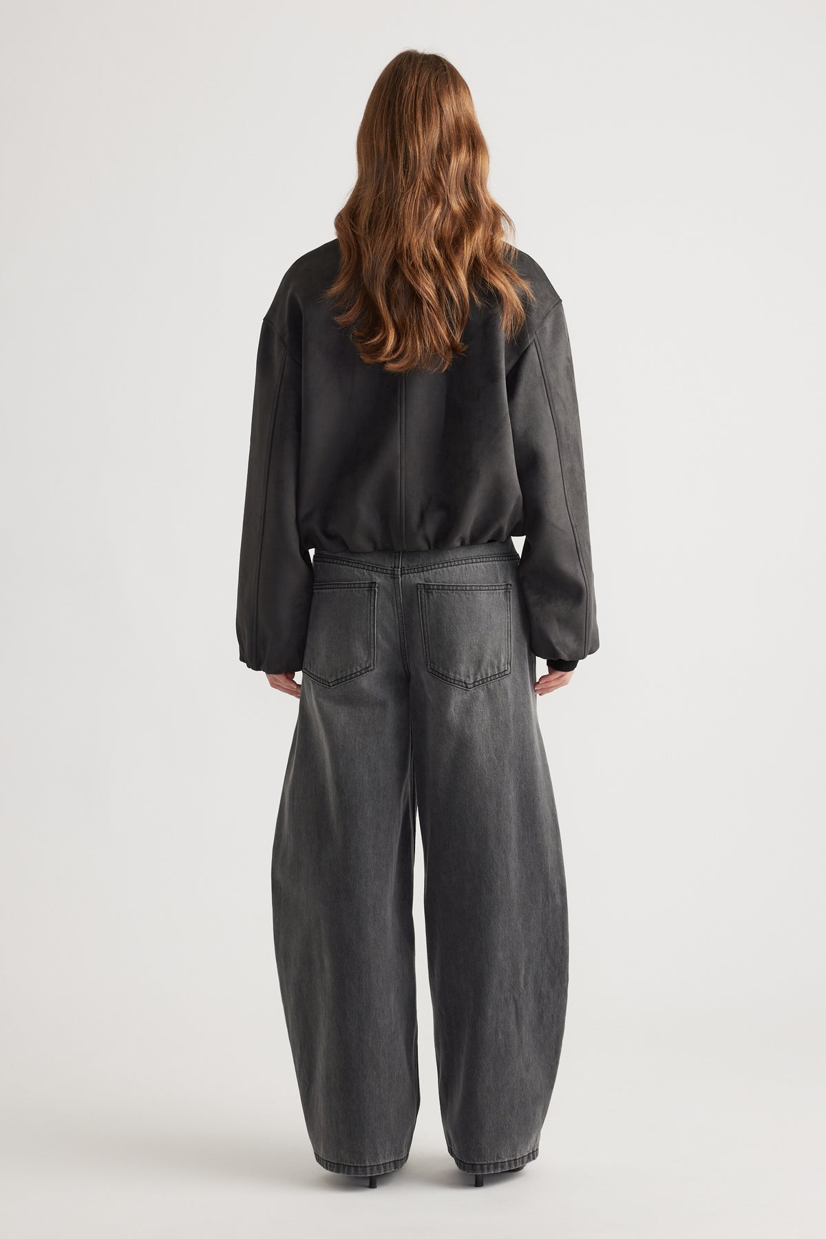 Back view of woman wearing Eden Faux Suede Bomber Jacket in charcoal paired with loose black wide-leg jeans