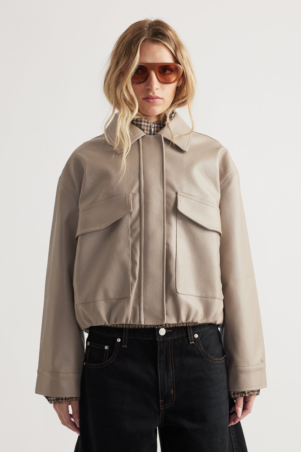Taupe faux leather jacket with oversized flap pockets and a relaxed fit, styled with dark denim jeans.