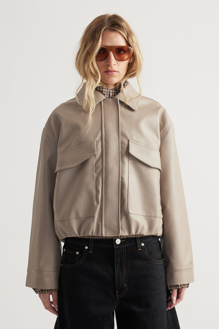 Taupe faux leather jacket with oversized flap pockets and a relaxed fit, styled with dark denim jeans.