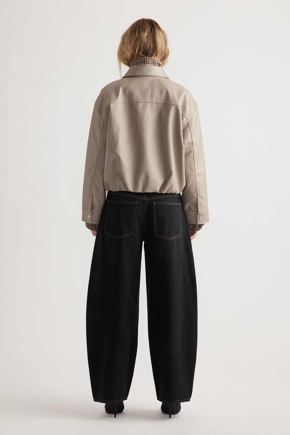 Back view of taupe faux leather jacket paired with relaxed black wide-leg jeans for a modern casual look.
