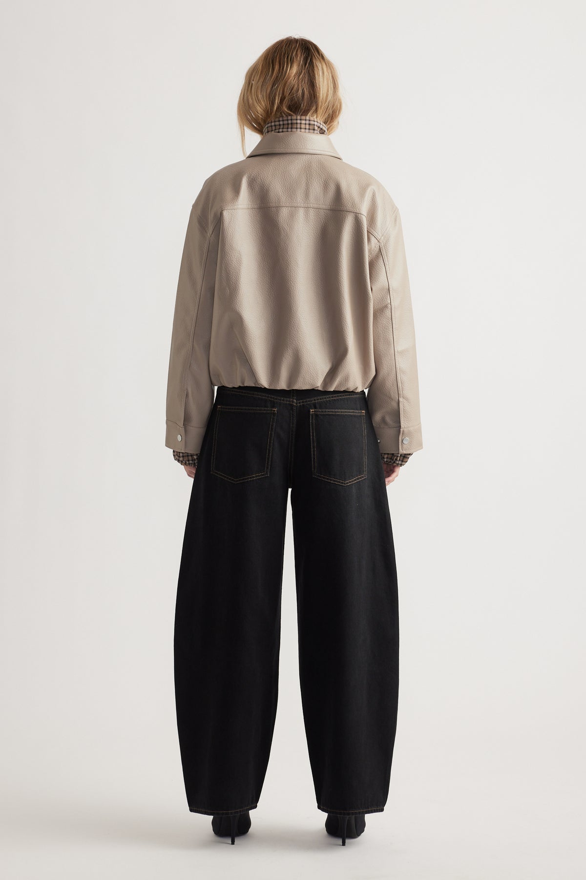Back view of taupe faux leather jacket paired with relaxed black wide-leg jeans for a modern casual look.
