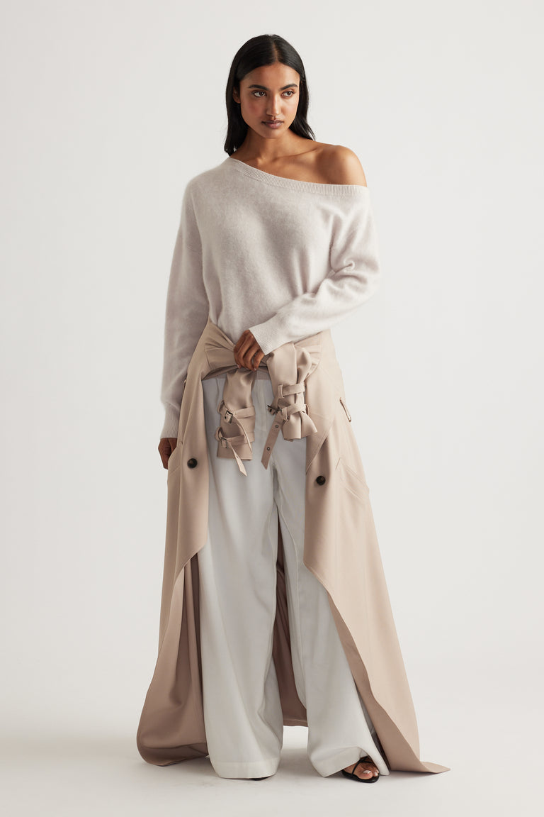 Woman wearing soft beige off-shoulder wool jumper paired with wide-leg white pants and a tied trench coat at the waist