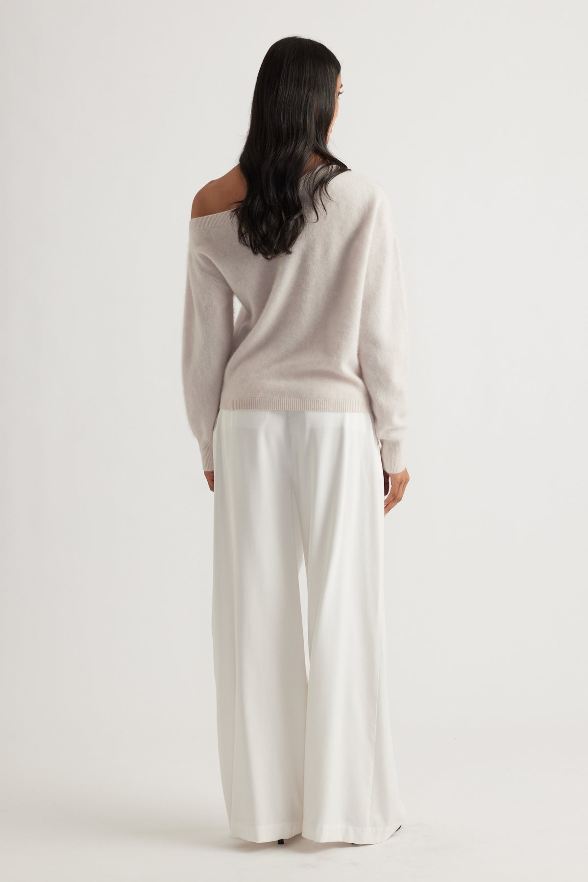Back view of woman wearing a soft sand-colored wool jumper with wide-leg white trousers for an elegant look