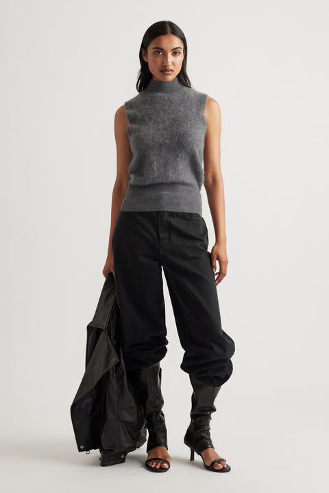 Woman wearing a sleeveless charcoal knit vest paired with loose black pants, heeled sandals, and holding a leather jacket