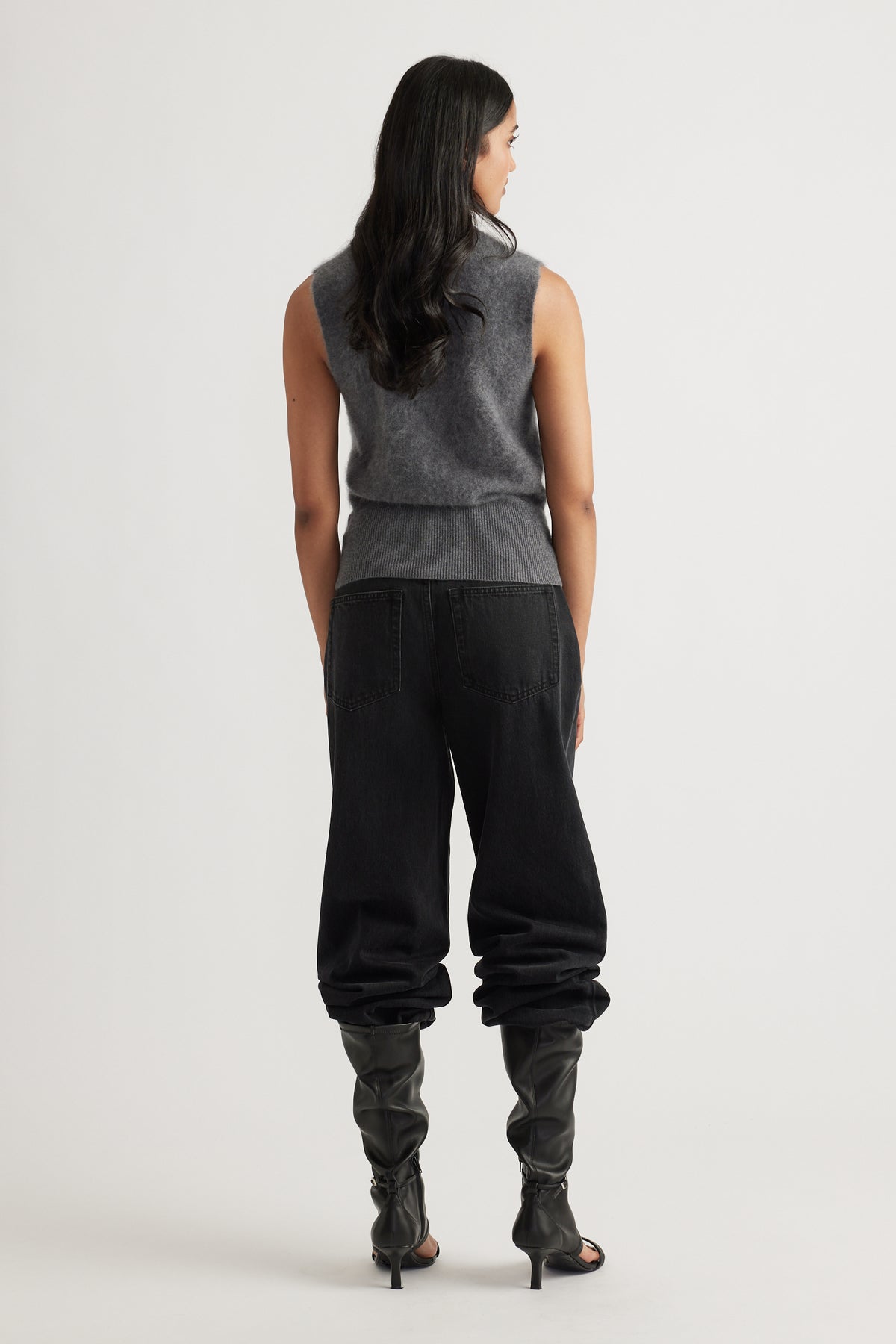 Back view of woman wearing a charcoal sleeveless wool knit vest paired with black relaxed-fit pants and heeled boots