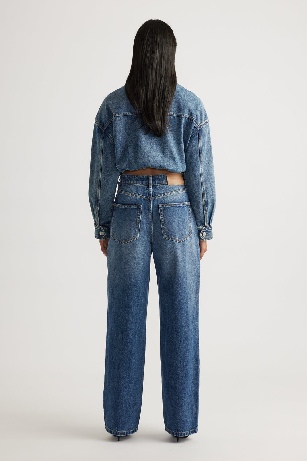Rear view of woman wearing high rise straight leg denim jeans paired with a cropped denim jacket