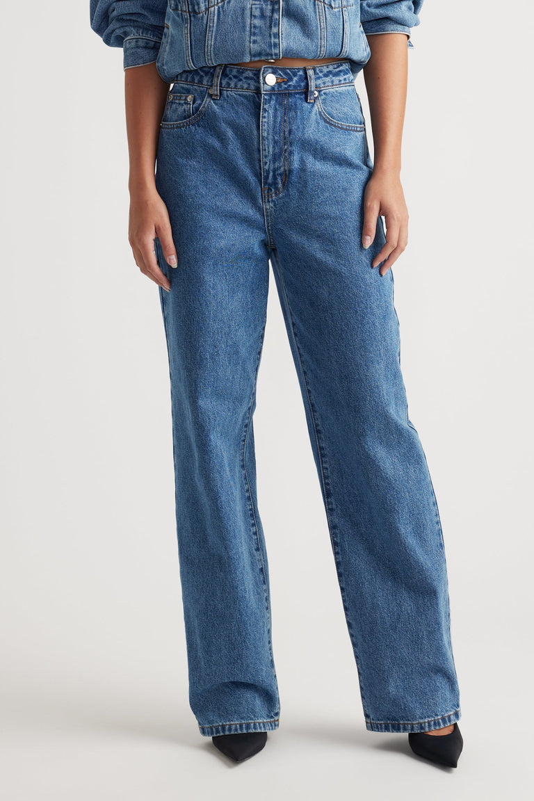 Woman wearing high-rise blue straight leg jeans paired with a denim shirt and black pointed shoes