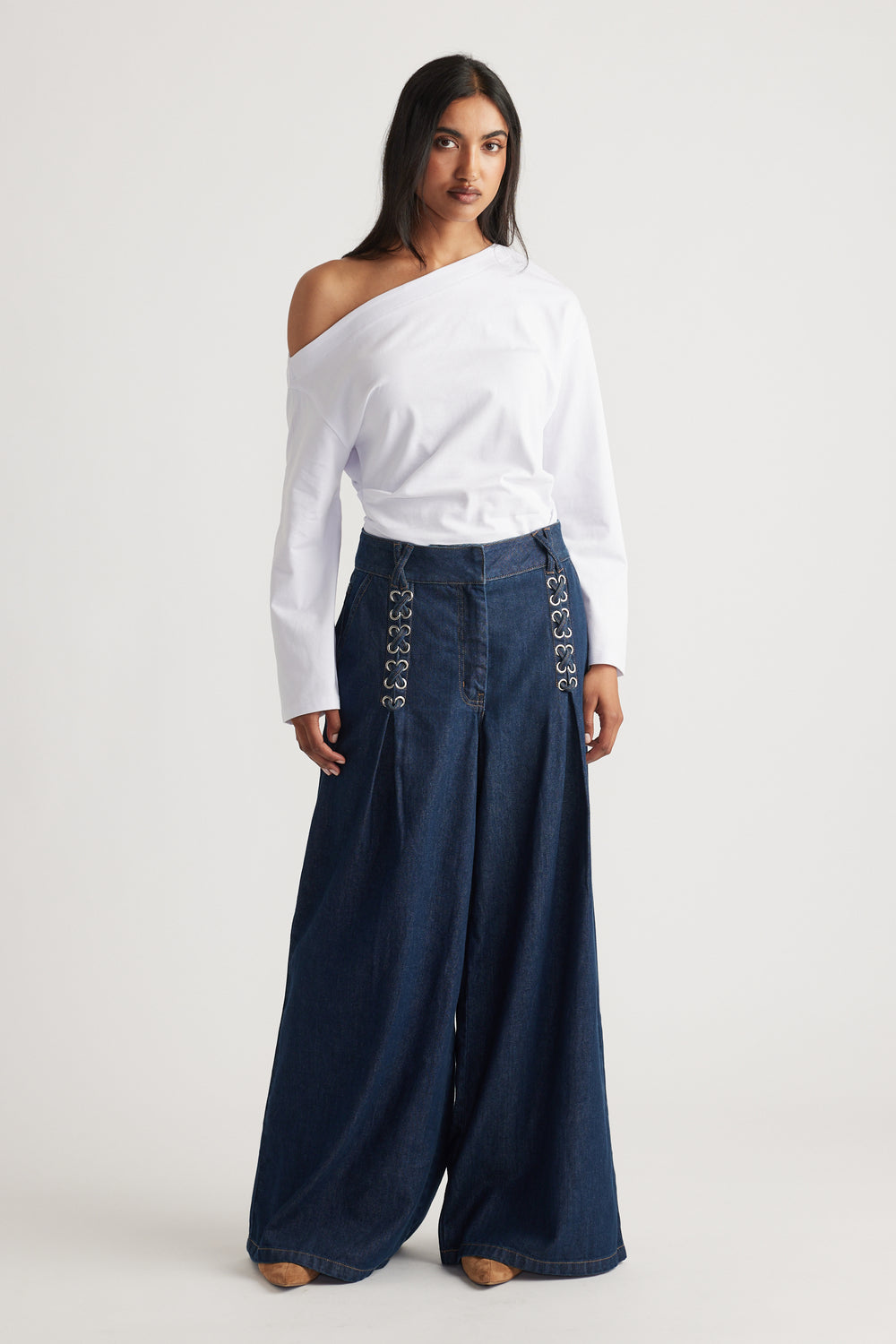 Woman wearing dark wide-leg denim pants with lace-up details paired with an off-shoulder white top