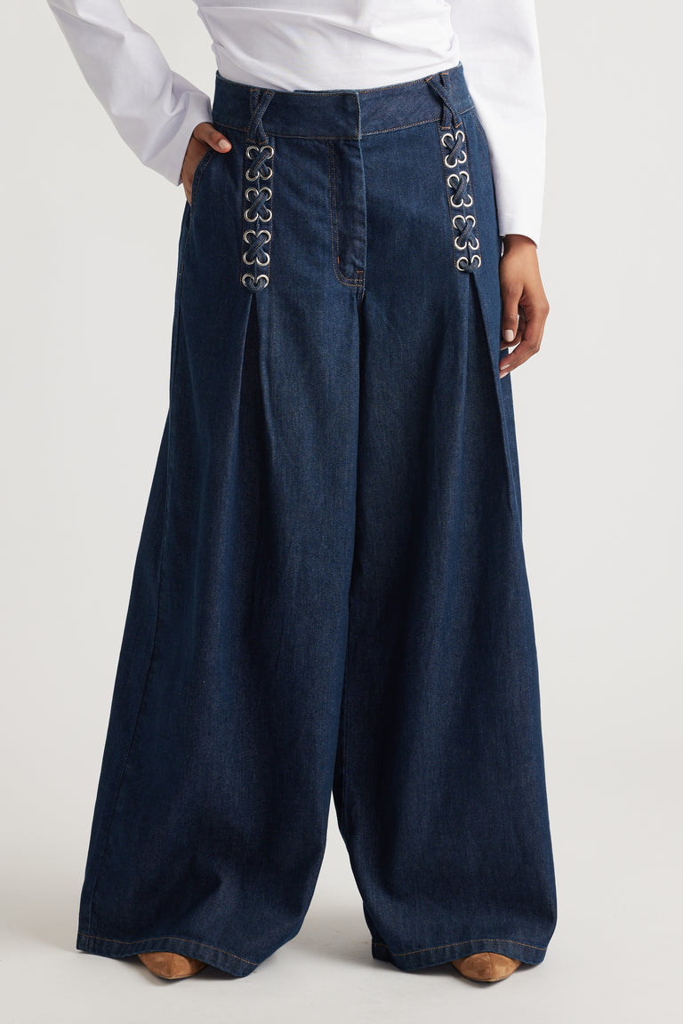 Woman wearing wide-leg dark indigo denim jeans with decorative metal eyelets near the waist and side pockets