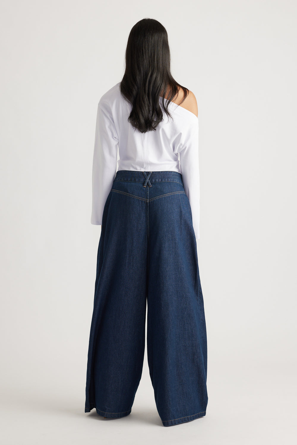 Woman shown from behind wearing dark wide-leg denim jeans paired with an off-shoulder white top