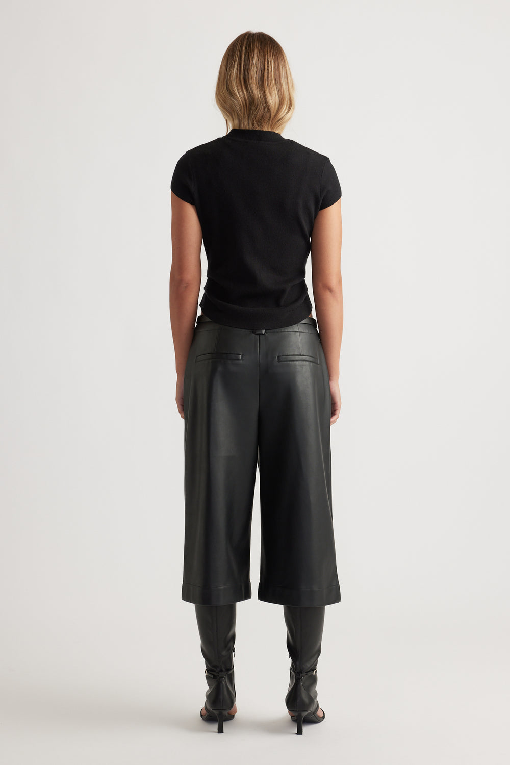 Back view of Lily Pleat Detail Knit Tee in black, paired with wide-leg cropped leather pants and heeled boots.