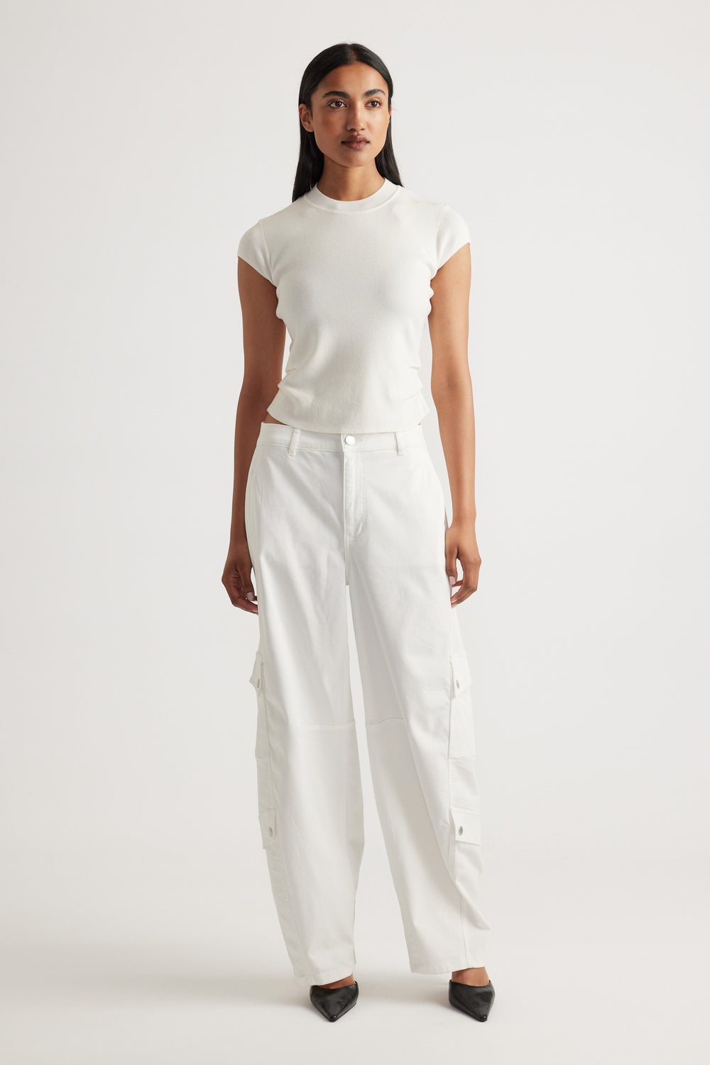 Woman wearing Lily Pleat Detail Knit Tee in soft winter white styled with relaxed white cargo pants and black pointed shoes by DECJUBA