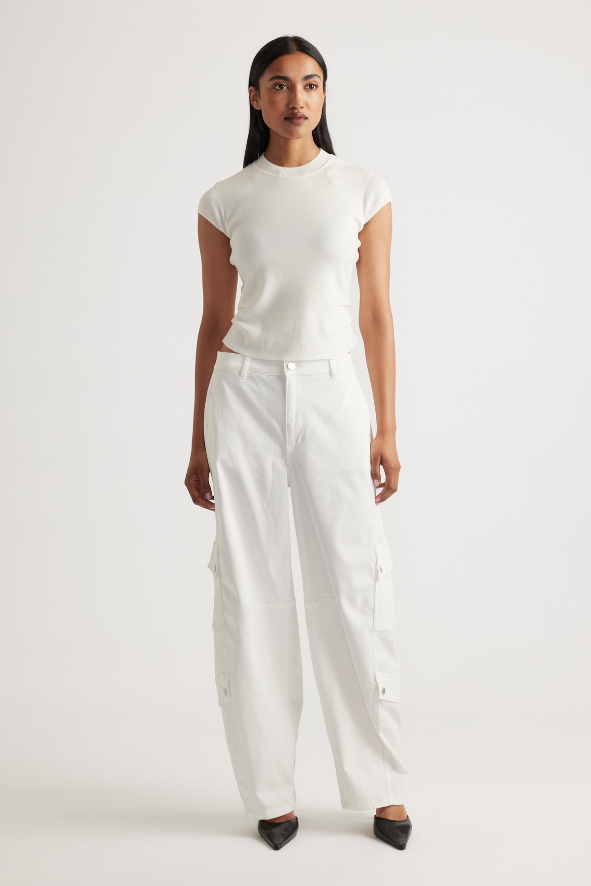 Woman wearing Lily Pleat Detail Knit Tee in soft winter white styled with relaxed white cargo pants and black pointed shoes by DECJUBA