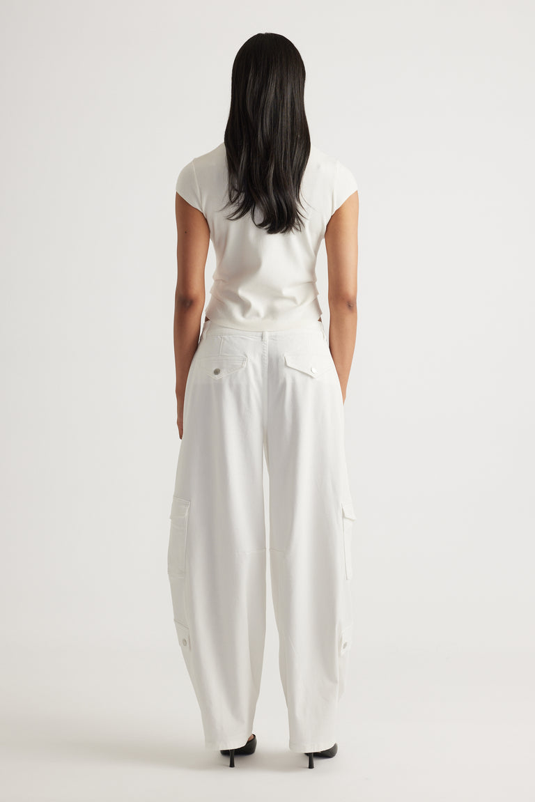Rear view of a woman wearing the Lily Pleat Detail Knit Tee in soft winter white paired with wide-leg white pants by DECJUBA