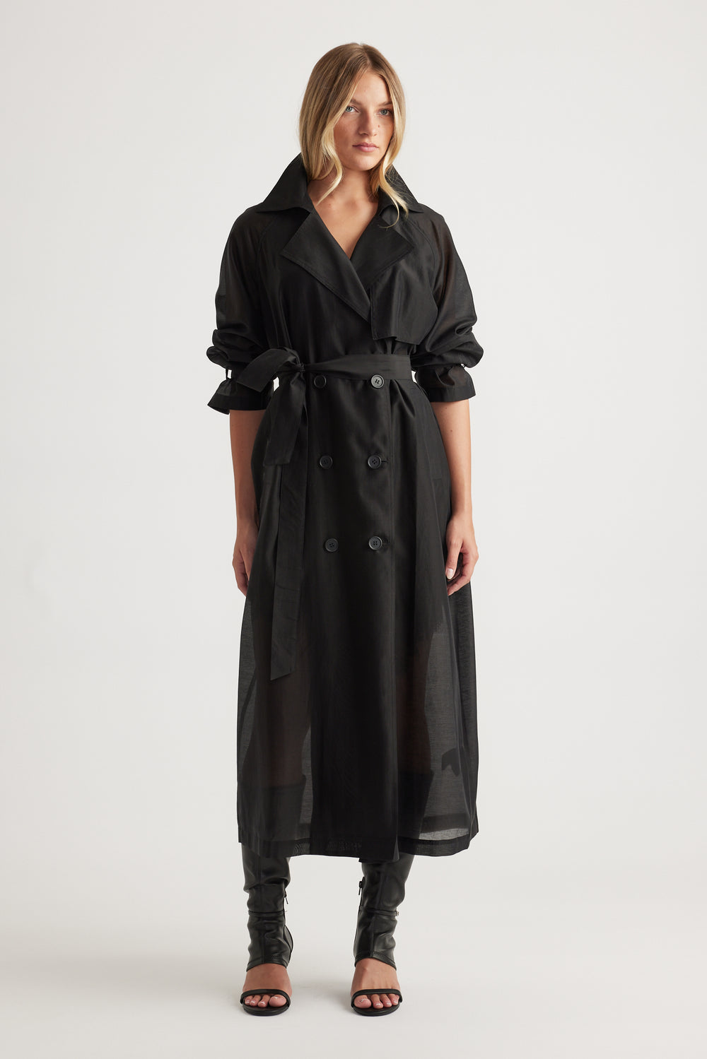 Woman wearing Briar Sheer Trench Coat in black with double-breasted front, belted waist, and rolled-up sleeves by DECJUBA