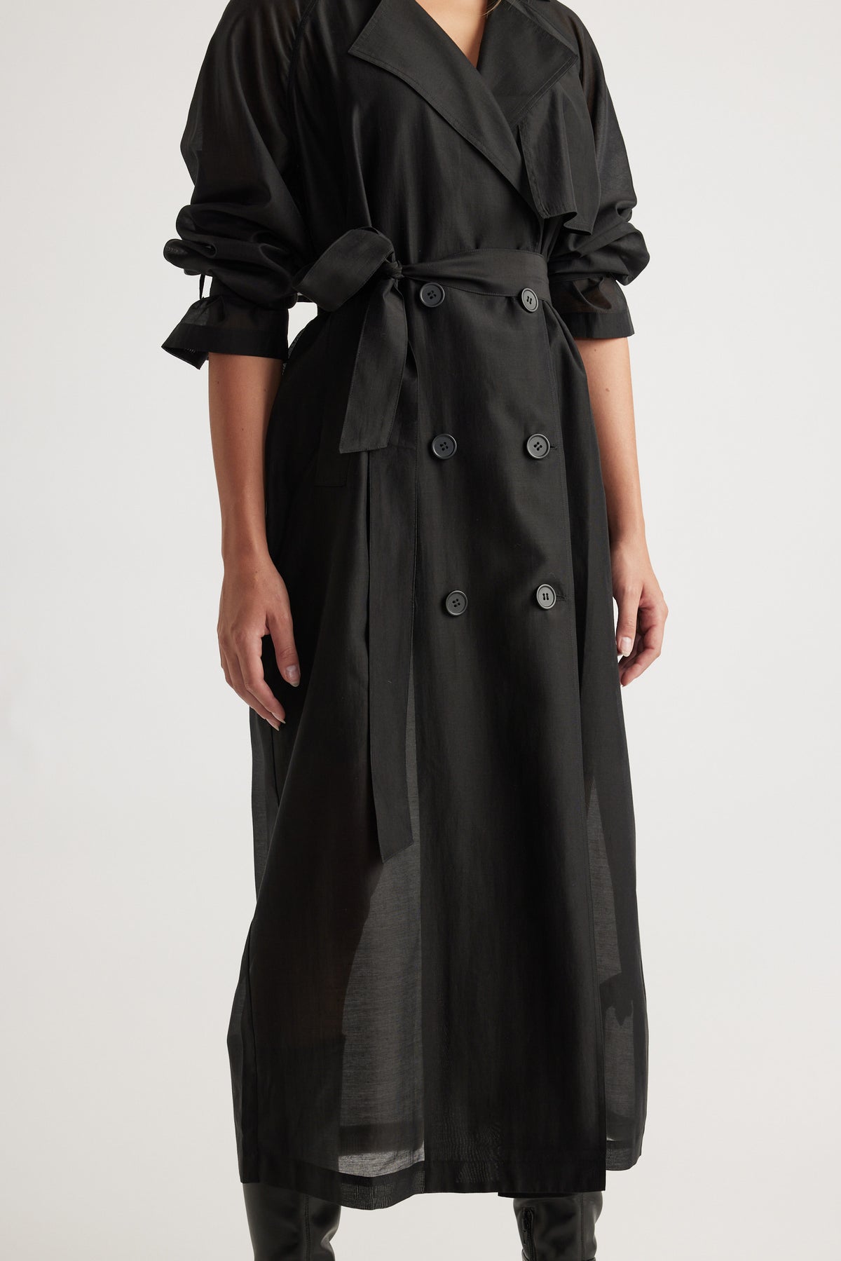 Woman wearing Briar Sheer Trench Coat in black with double-breasted buttons, belted waist, and ruched sleeves by DECJUBA