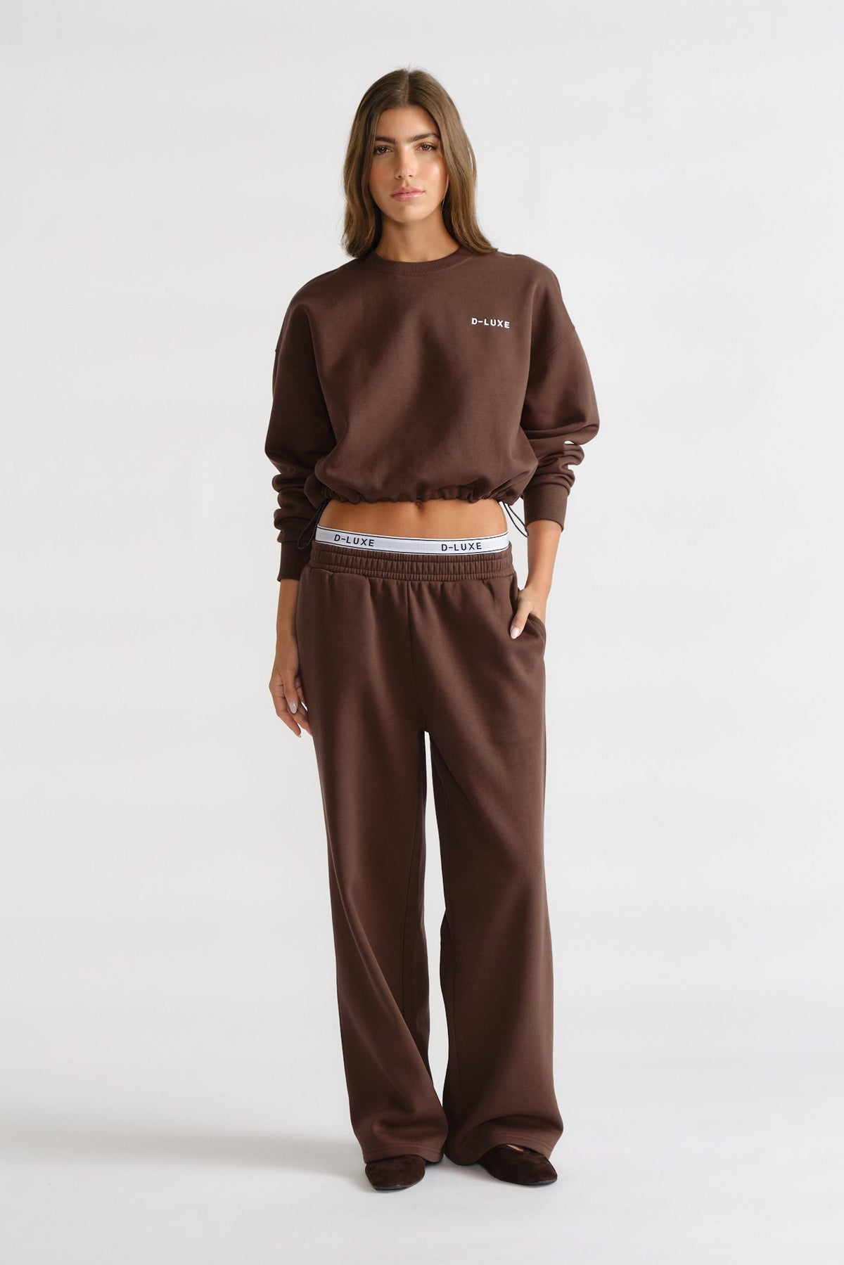 Woman wearing a relaxed dark brown sweat set with elasticized waistband trackpants and a cropped sweatshirt with minimal logo detail