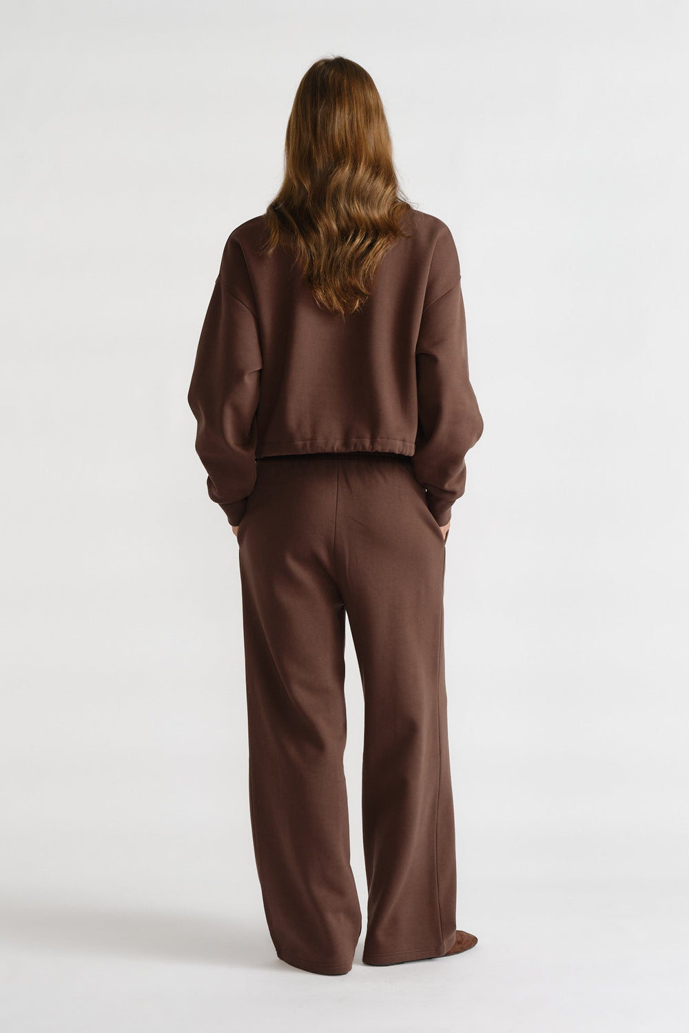 Rear view of a woman wearing relaxed-fit brown trackpants and a matching loose sweatshirt for a comfortable casual look.
