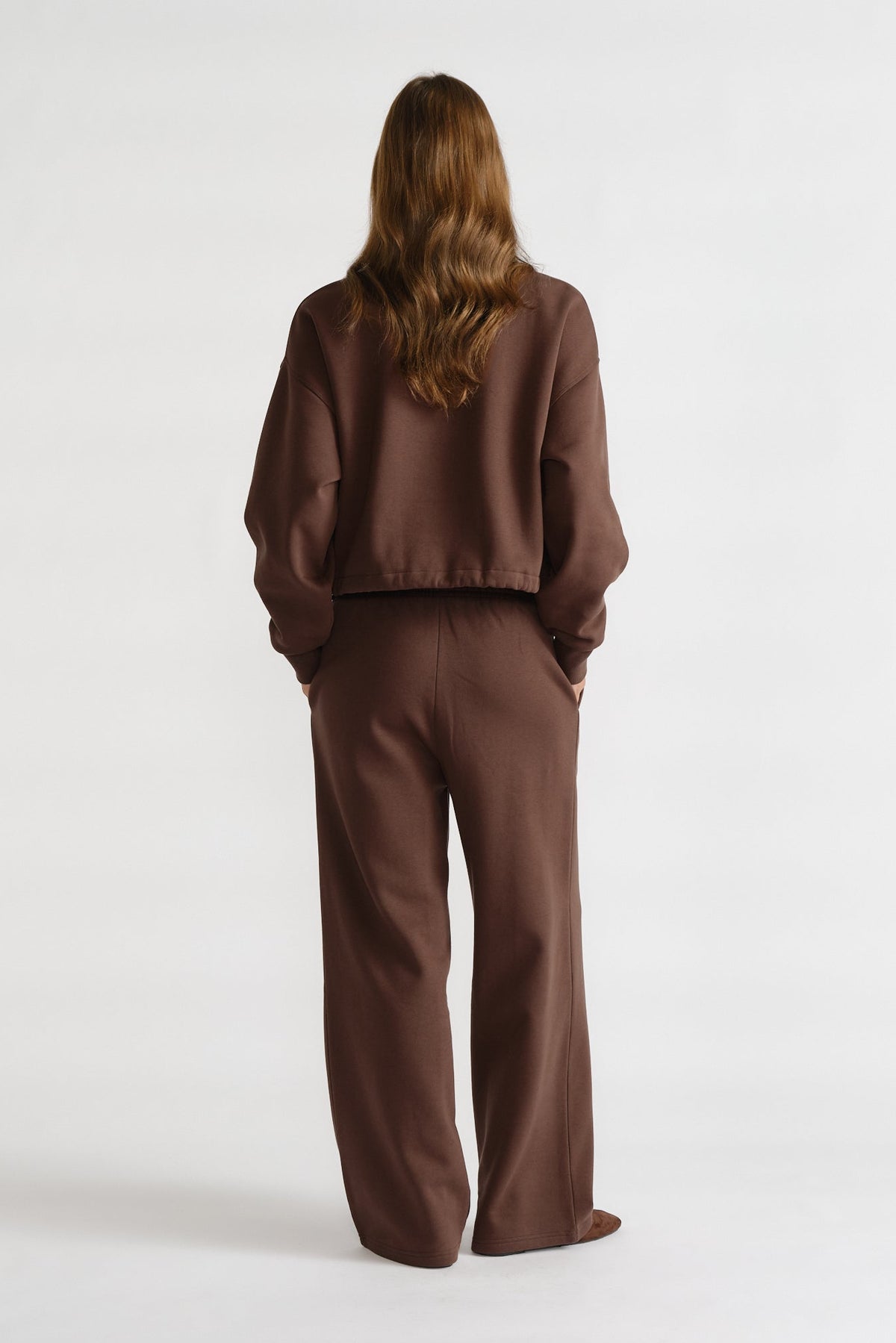 Rear view of a woman wearing relaxed-fit brown trackpants and a matching loose sweatshirt for a comfortable casual look.