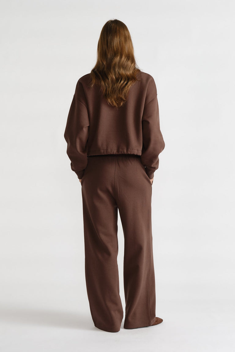 Rear view of a woman wearing relaxed-fit brown trackpants and a matching loose sweatshirt for a comfortable casual look.