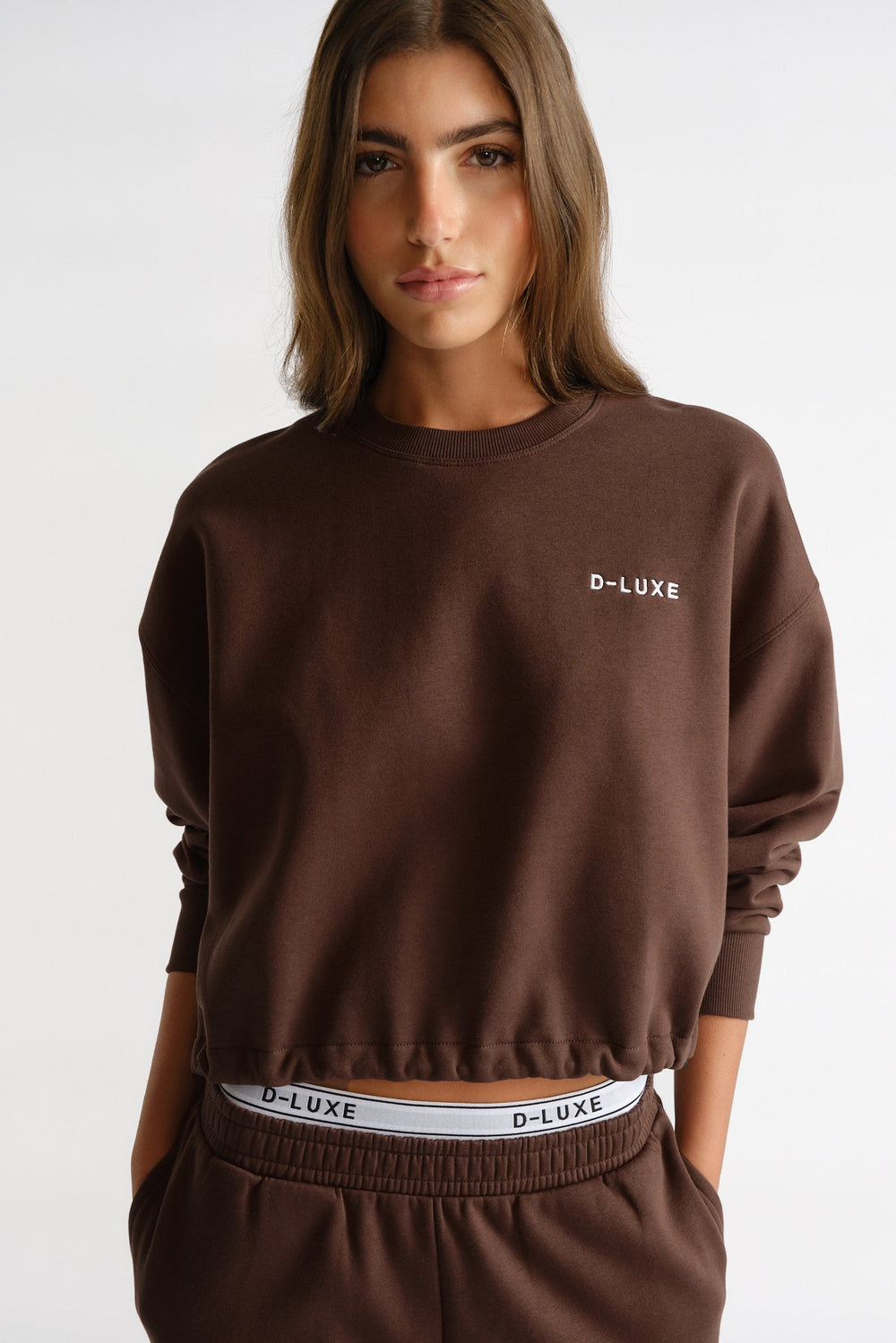 Woman wearing a rich brown D-Luxe Logo Crop Sweat with relaxed fit and matching waistband for a casual, stylish vibe.
