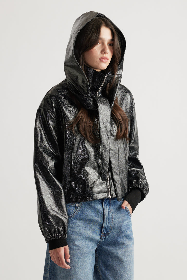 Woman wearing a glossy black hooded jacket with a front tie detail, styled with relaxed mid-blue denim jeans.