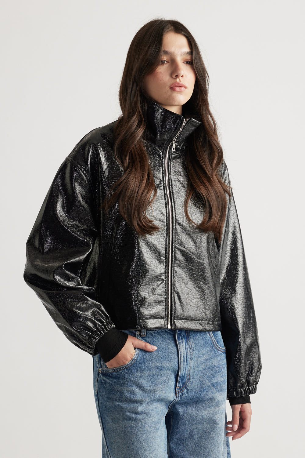 Woman wearing a shiny black zip-up jacket with a high collar and relaxed fit, paired with classic blue jeans