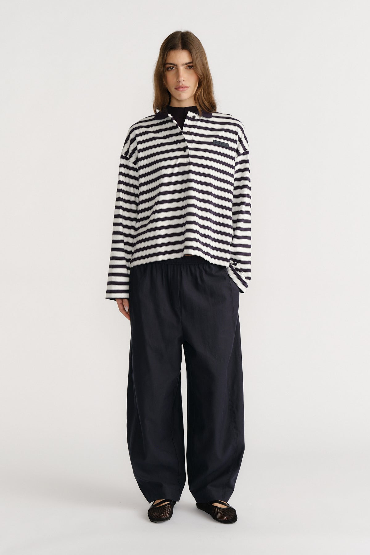 Woman wearing a relaxed striped long-sleeve polo top paired with loose wide-leg black trousers and black flats.