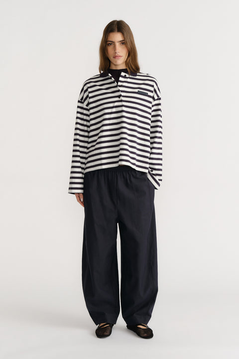Woman wearing a relaxed striped long-sleeve polo top paired with loose wide-leg black trousers and black flats.