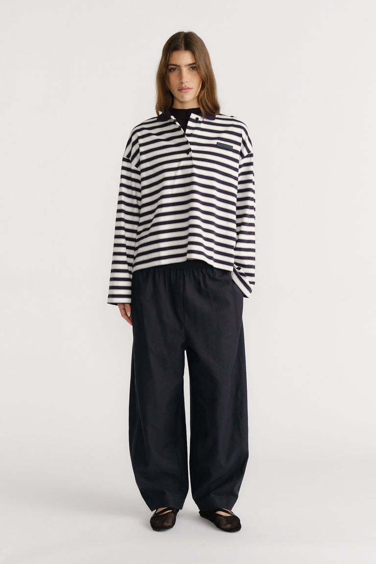 Woman wearing a relaxed striped long-sleeve polo top paired with loose wide-leg black trousers and black flats.