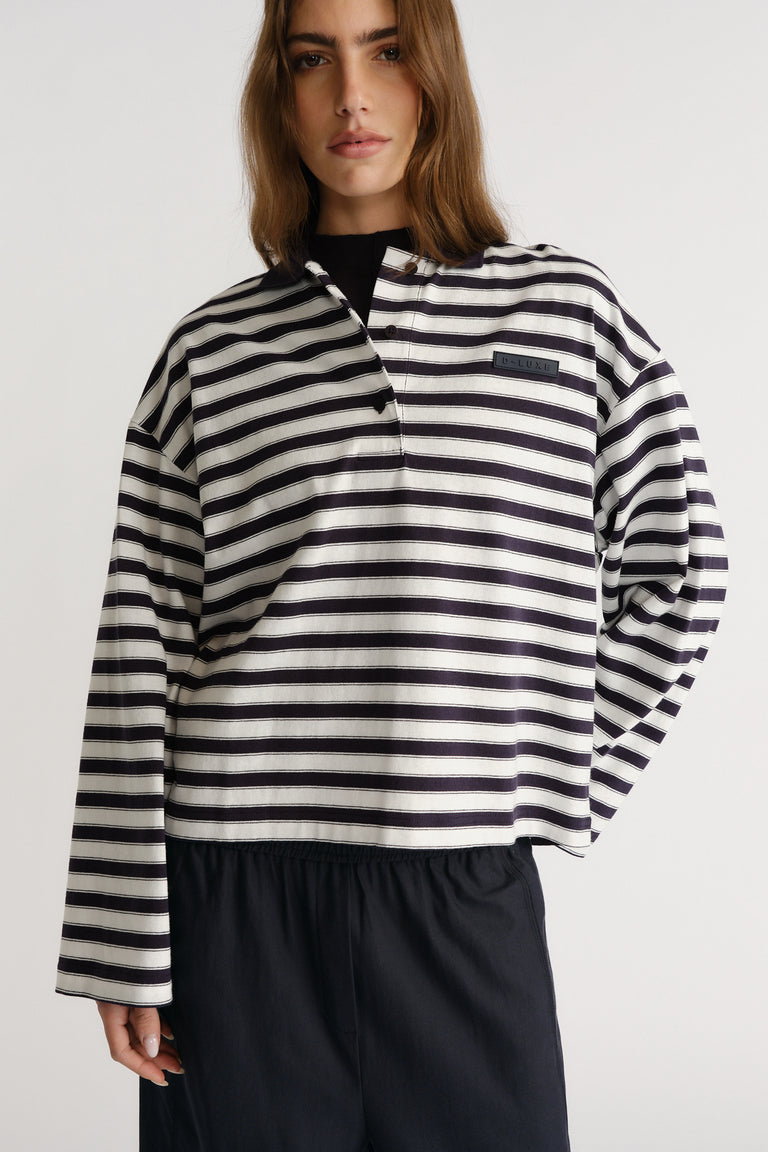Woman wearing a relaxed fit navy and white striped polo with long sleeves and a subtle logo patch on chest.