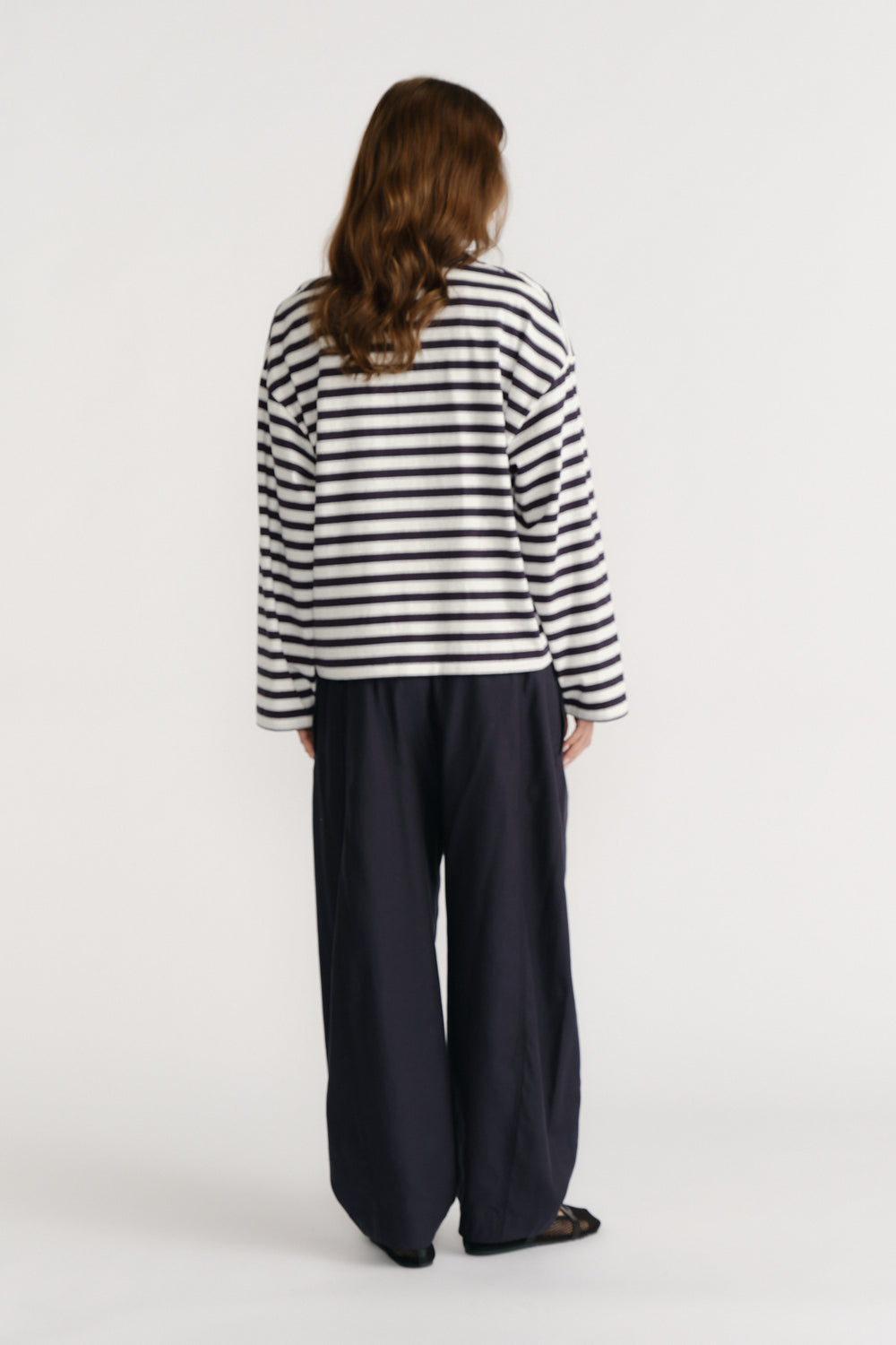 Woman wearing a relaxed fit navy and white striped top paired with loose navy wide-leg pants and black sandals viewed from behind
