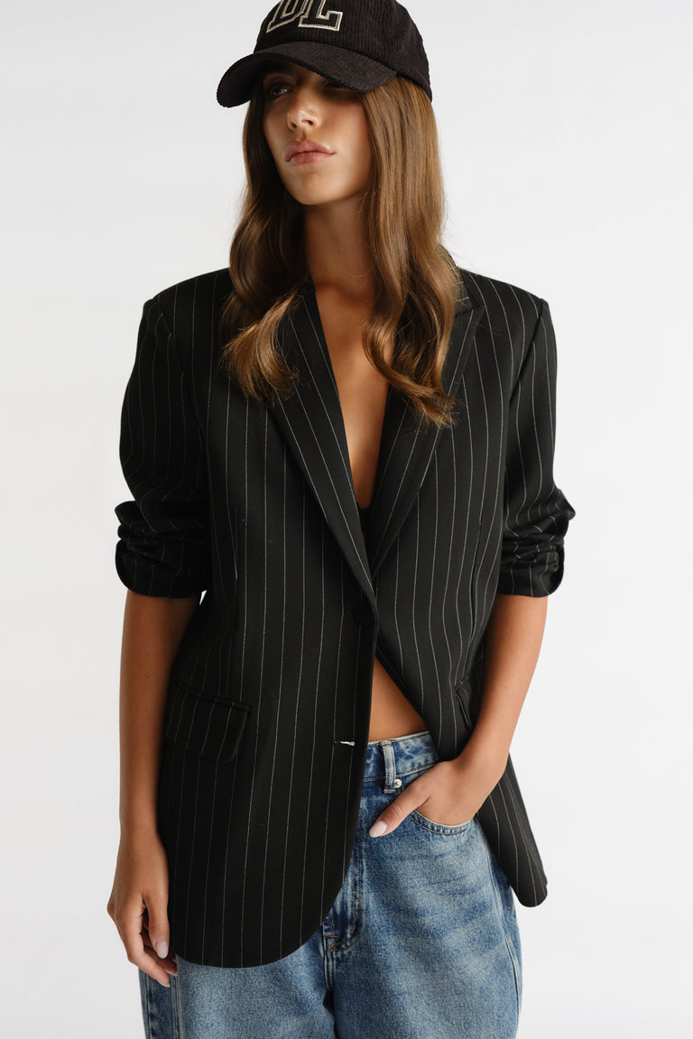 Woman wearing a black corduroy D-luxe Kim Cord Cap paired with a pinstripe blazer and casual blue jeans for a chic look