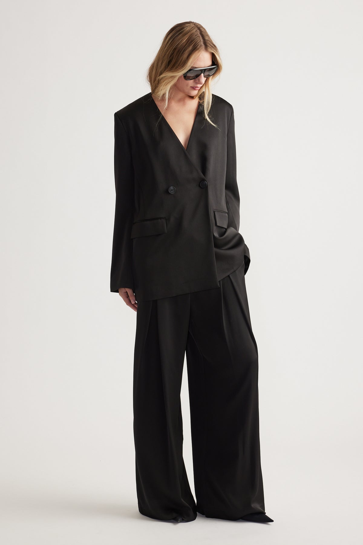 Woman wearing black wide leg pants paired with an oversized double-breasted blazer and sunglasses.