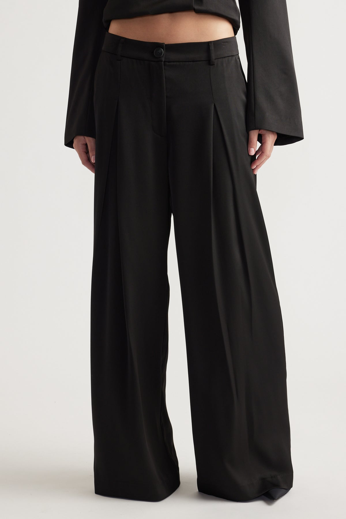 High-waisted black wide-leg pants with a front button and pleated detail for a relaxed fit.